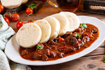 Traditional Czech Goulash meal with dumplings on plate on wood table, beer.