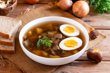 Bowl of mushroom soup with fresh mushrooms and eggs. Served in a white bowl on rustic table. Dinner concept.