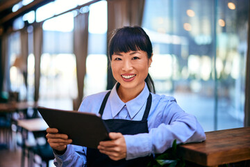 Portrait of a smiling Asian waitress, holding a digital tablet, smiling for the camera.