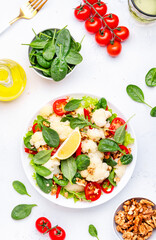 Fresh vegan cauliflower salad with baked red paprika, cherry tomatoes, spinach with walnuts on white table background, top view