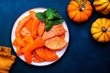 Healthy sweet snack. Baked pumpkin caramelized in orange glaze, autumn or winter dessert food on dark blue table background. Top view