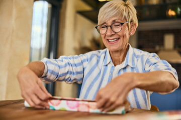 A happy senior woman packing a book for a gift, for her friend.
