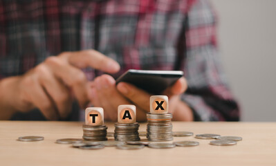 concept of finance, income, taxes ,costs and expenses .Stacked coins and wooden blocks with text TAX. Calculating income or expenses to fill out personal income tax payment forms to government agency
