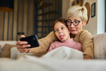 A grandma and her grandchild making funny faces while taking photos with a mobile phone.