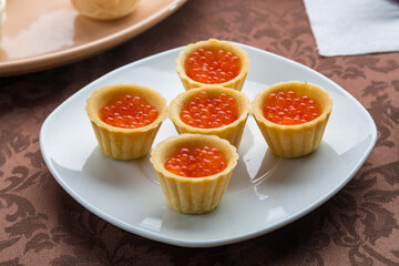 Red caviar in tartlets on a plate on a brown tablecloth. Horizontal