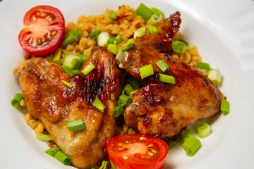 Chicken wings baked with bulgur, colored with green onions on a white plate, close-up