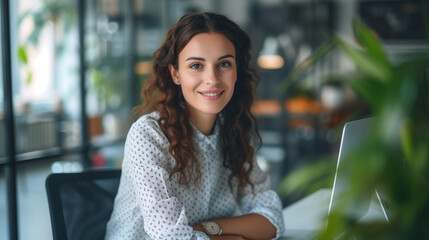 Smiling young woman with curly hair at her computer in a modern office with greenery