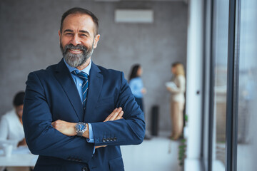 Portrait of smiling mid adult businessman standing at corporate office. Portrait of mature businessman at modern office. Happy mature business professional standing in modern office.