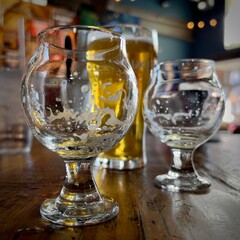 Shallow focus close-up on empty beer glass, with soft focus on more glasses, beer, and bar in background