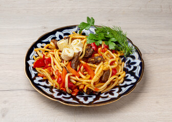 Fried lagman, noodles with meat and vegetables in a traditional plate on a wooden background