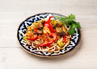 Uyghur lagman, noodles with meat and vegetables in a traditional plate on a wooden background