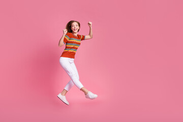 Fototapeta na wymiar Full size photo of delighted pretty girl jump raise fists shout yeah empty space isolated on pink color background