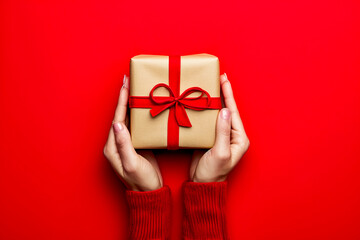 Hand holding wrapped gift with bow on top and woman in red wearing striped sweater.