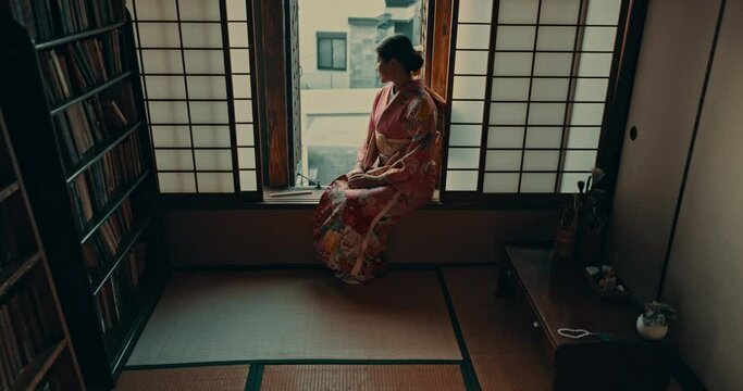 Thinking, culture and traditional japanese woman by window for reflection, calm and wellness in morning. Kimono, happy and person in home with view for thoughtful, wondering and relax in living room