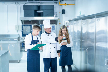 Senior male chef teaches young teenage boys cooking in school kitchen. Education Concept