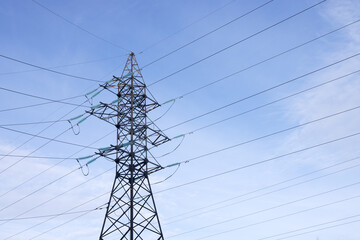 A high-voltage mast with wires on a background of blue sky with light clouds. Bottom view. - obrazy, fototapety, plakaty