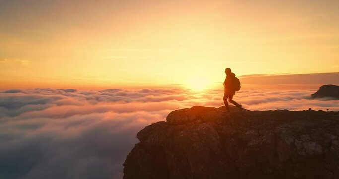 Young female girl hiker walks at mountain top above the clouds. Golden sunset and silhouette of tourist