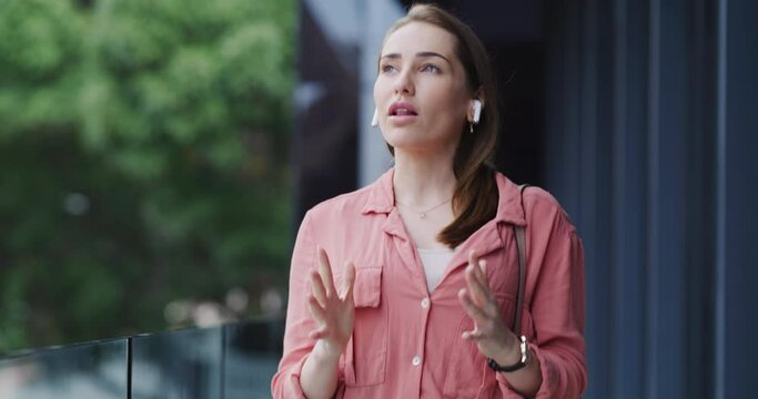 Ear buds, conversation and woman in the city walking and talking for business deal or partnership. Communication, working and professional young female person speaking on mobile discussion in town.