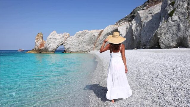 A elegant tourist woman in a white summer dress walks along the beautiful beach of Lalaria, Skiathos island, Greece