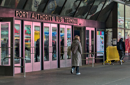 People pass in front of the sign for the Port Authority Bus Terminal transportation hub on 8th Avenue and 42nd Street in Midtown, Manhattan, New York City.