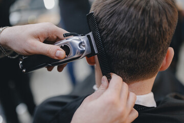 Closeup master barber hairdresser does hairstyle with hair clipper and comb. Concept banner...