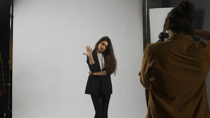 Fototapeta premium Backstage of model and professional team in the studio. Full length of attractive model in suit posing, photographer taking pics, cool expression.