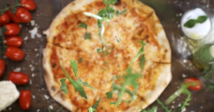 Super slow motion macro of fresh green rocket leaves falling on traditional italian dish of pizza margherita with tomato sauce and mozzarella cheese in rustic restaurant kitchen at 1000 fps.