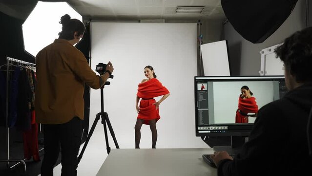Model and production team in the studio. Photographer helps shows model with poses, editor assistant sitting at the desktop checks pics real time.