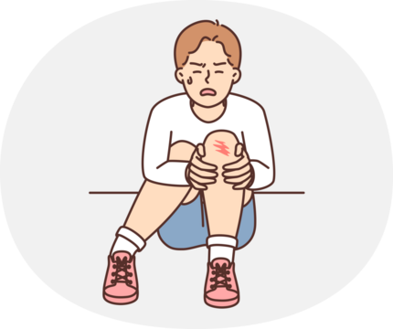 Crying teenager boy sits on ground and holds on to injury on knee after fall during walk. Unfortunate child was injured during sports activities or active games with friends