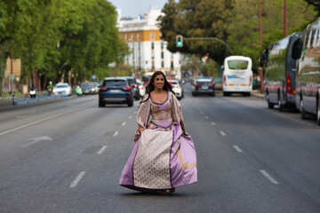 Beautiful Latin woman with long curly hair dressed in a 15th century dress running between cars on a big city avenue. The woman travels in time from the past to the present.