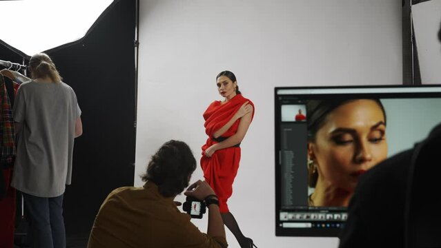 Model and production team in the studio. Female model posing for photographer, editor table at the side with desktop screen with pictures real time.