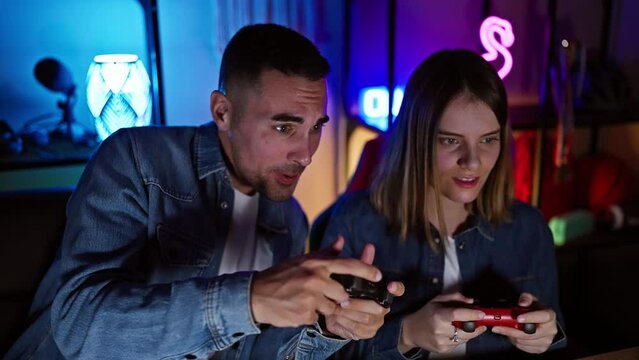 A man and woman intensely play video games together in a neon-lit home gaming room at night.