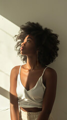 Fototapeta premium Radiant Glow: A Young Black Woman Stands Near a Sunlit Wall in a White Room, Bathed in Soft Bright Light