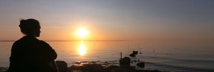 Silhouette of a lonely grieving girl sitting by the ocean at sunset, grief, farewell, memorial