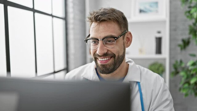 Confident young hispanic man working as a doctor at the clinic, smiling behind the computer