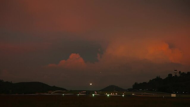 Airplane landing in the evening, long shot. Fiery sunset sky over the airport. Runway landing lights