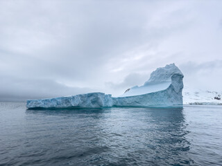 A huge high breakaway glacier drifts in the southern ocean off the coast of Antarctica at sunset, the Antarctic Peninsula, the Southern Arctic Circle, azure water, cloudy weather