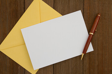 Blank greeting card with yellow envelope and pen on wood