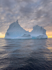 A huge high breakaway glacier drifts in the southern ocean off the coast of Antarctica at sunset, the Antarctic Peninsula, the Southern Arctic Circle, azure water, cloudy weather