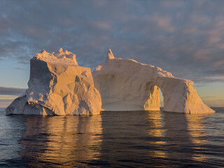 A huge high breakaway glacier drifts in the southern ocean off the coast of Antarctica at sunset, the Antarctic Peninsula, the Southern Arctic Circle, azure water, cloudy weather