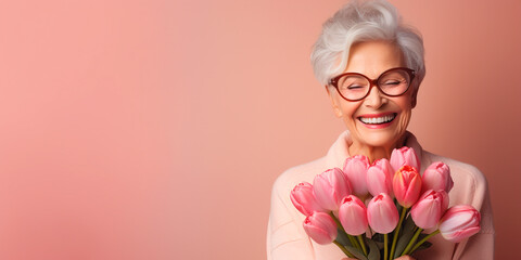 Joyful, happy grandmother in glasses and a sweater on a pink background with a bouquet of tulips, copy space