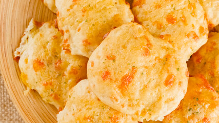 Cheese biscuits with butter and garlic seasoning topping close-up on a wooden plate, flat lay