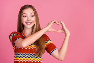 Photo of cheerful lovely girl toothy smile arms fingers demonstrate heart symbol empty space isolated on pink color background