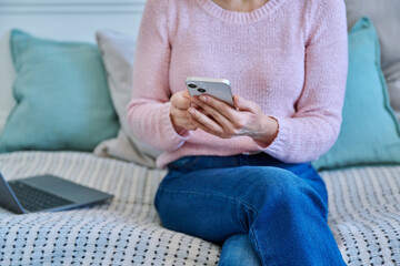 Close-up of smartphone in hands of woman sitting on couch at home