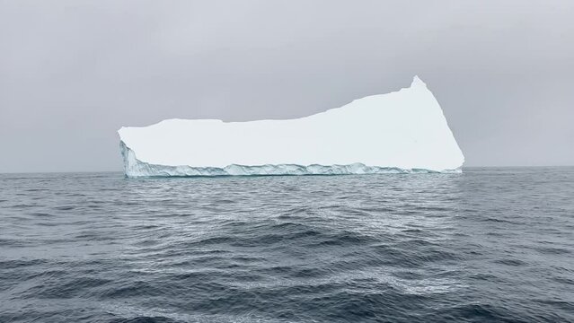 A huge high breakaway glacier drifts in the southern ocean off the coast of Antarctica at sunset, the Antarctic Peninsula, the Southern Arctic Circle, azure water, cloudy weather