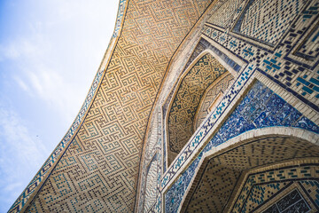 Element of the facade of a madrasah made of brick with mosaic cladding in the ancient city of Bukhara in Uzbekistan, architecture in oriental style, facade of a mosque with patterns and ornaments - obrazy, fototapety, plakaty