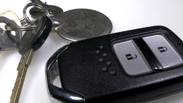 Closeup dolly shot of a set of traditional keys on a keyring, next to an electronic wireless remote control keyless fob for a vehicle.