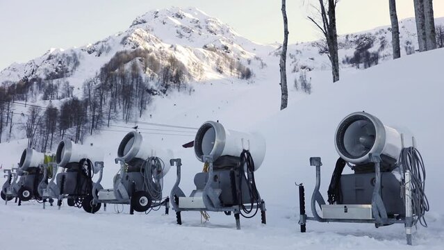 Row of snow canons on slope of resort, slow motion.