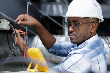 a man electrician in uniform and helmet checking voltage