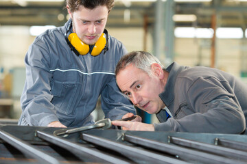 two industrial workers inspecting work piece standing on the fac